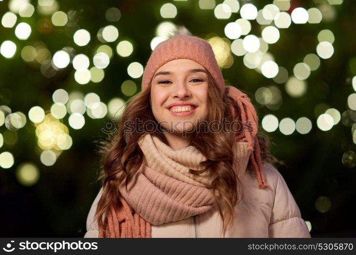 holidays and people concept - portrait of beautiful happy young woman over christmas tree lights in winter evening. happy young woman over christmas tree lights