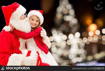 holidays and people concept - santa claus with happy little girl over christmas tree background. santa claus with happy girl over christmas tree