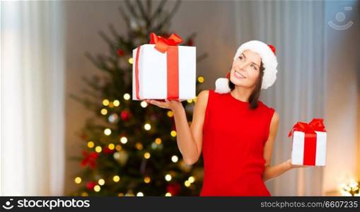 holidays and people concept - smiling woman in santa helper hat with gift boxes over christmas tree lights background. smiling woman in santa hat with christmas gifts