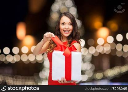 holidays and people concept- smiling woman with gift box over night christmas tree lights background. woman with gift box over christmas tree lights