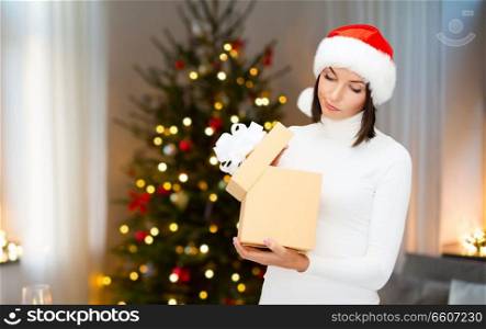 holidays and people concept - woman in santa helper hat opening gift box over christmas tree lights background. smiling woman in santa hat with christmas gift