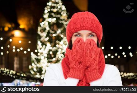 holidays and people concept - young woman in winter clothes over christmas tree lights background. young woman in winter clothes over christmas tree