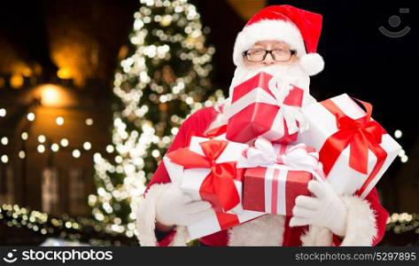 holidays and presents concept - close up of santa claus with gifts over christmas tree background. close up of santa claus with christmas gifts