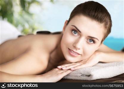 holidays and spa concept - beautiful woman in spa salon with hot stones