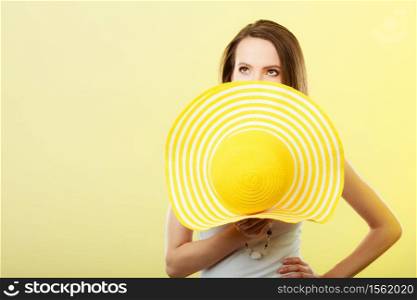Holidays and summer fashion. Woman covering her face with big yellow hat on bright background.