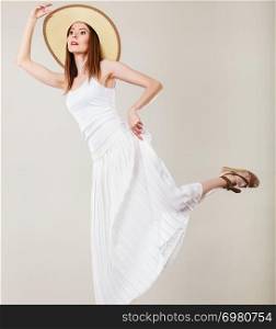 Holidays and summer fashion. Woman wearing big straw hat white dress. Female model posing on bright gray background.