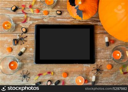 holidays and technology concept - pumpkins, candies, candles and tablet pc computer on wooden table. halloween pumpkins, candies, candles and tablet pc
