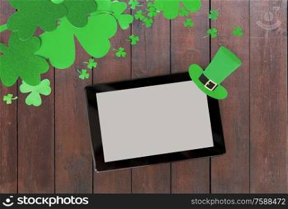 holidays and technology concept - tablet pc computer and st patricks day decorations made of paper on wooden background. tablet pc and st patricks day decorations on wood