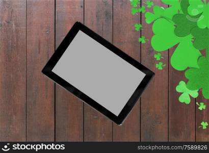 holidays and technology concept - tablet pc computer and st patricks day decorations made of paper on wooden background. tablet pc and st patricks day decorations on wood