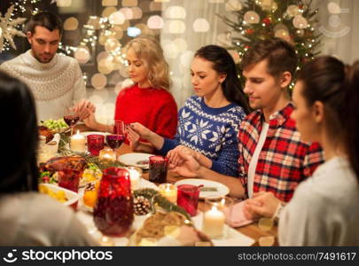 holidays and thankfulness concept - friends holding hands and praying while having christmas dinner at home. friends having home christmas dinner and praying