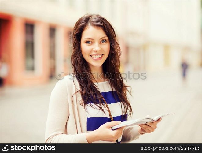 holidays and tourism concept - beautiful girl looking into tourist book in the city