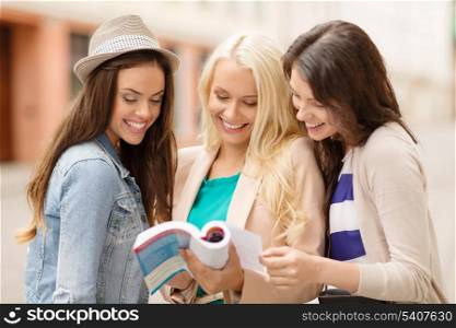 holidays and tourism concept - beautiful girls looking into tourist book in the city