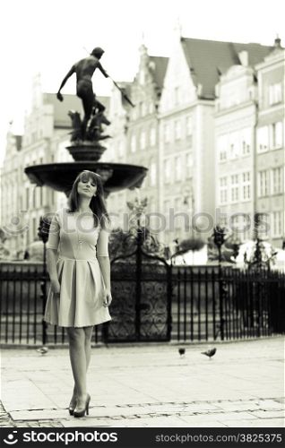 Holidays and tourism concept. Full length pretty woman in elegant dress outdoor on the street of the old town european city Gdansk Danzig Neptune fountain Poland. Blach white photo