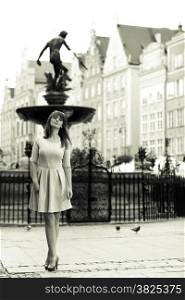 Holidays and tourism concept. Full length pretty woman in elegant dress outdoor on the street of the old town european city Gdansk Danzig Neptune fountain Poland. Blach white photo