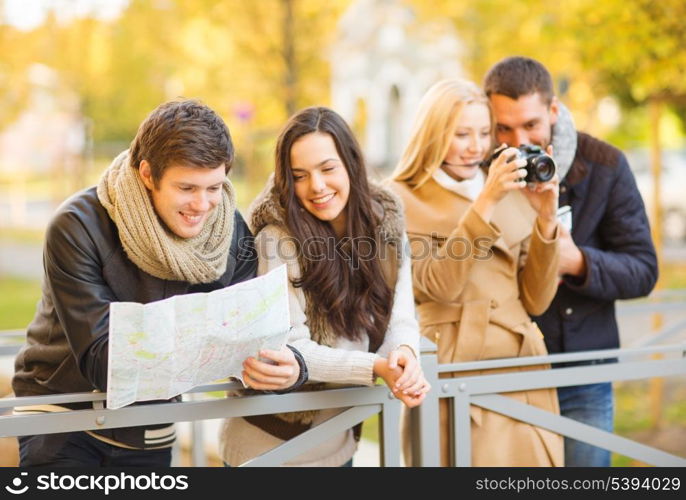 holidays and tourism concept - group of friends or couples with tourist map and camera in autumn park