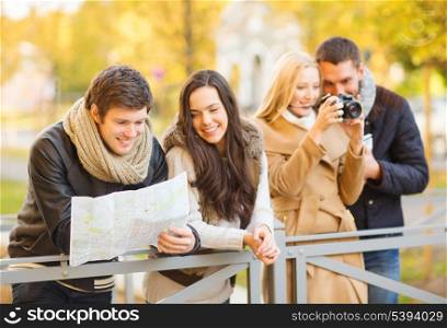 holidays and tourism concept - group of friends or couples with tourist map and camera in autumn park