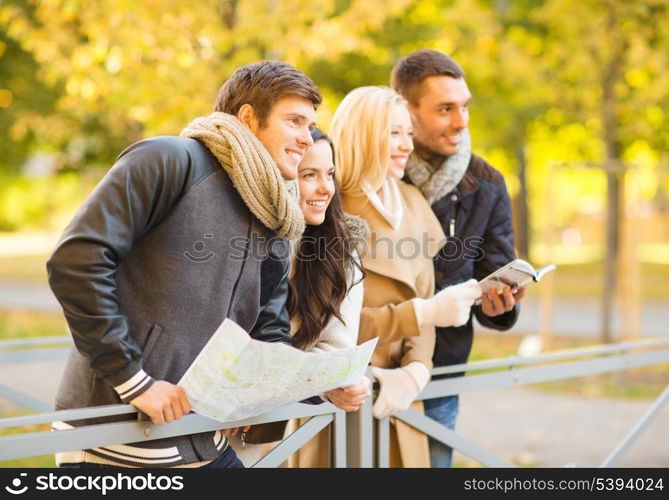 holidays and tourism concept - group of friends or couples with tourist map in autumn park