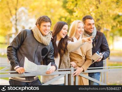 holidays and tourism concept - group of friends or couples with tourist map in autumn park