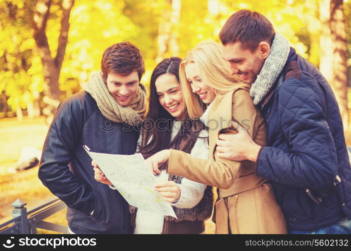 holidays and tourism concept - group of friends or couples with tourist map in autumn park