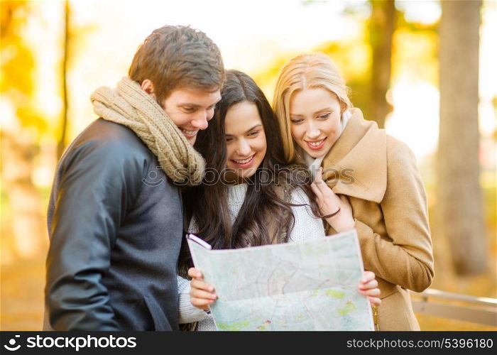 holidays and tourism concept - group of friends with tourist map in autumn park