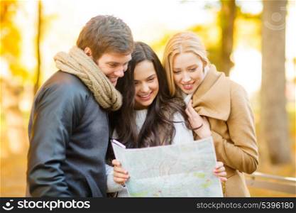 holidays and tourism concept - group of friends with tourist map in autumn park