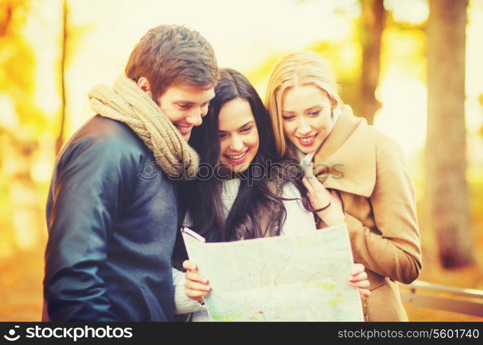 holidays and tourism concept - group of friends with tourist map in autumn park