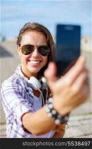 holidays and tourism concept - smiling teenage girl taking picture with smartphone camera aoutdoors