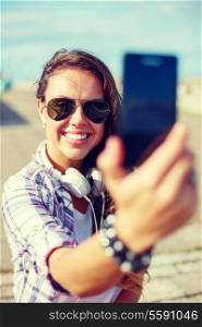 holidays and tourism concept - smiling teenage girl taking picture with smartphone camera outdoors