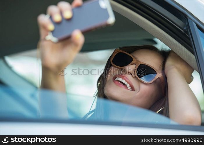 Holidays and tourism concept - smiling teenage girl taking selfie picture with smartphone camera outdoors in car