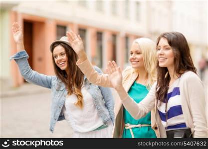 holidays and tourism concept - three beautiful girls waving hands in the city
