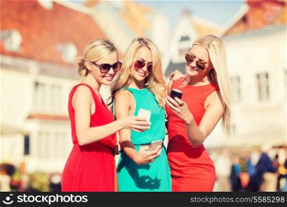 holidays and tourism, modern technology concept - beautiful blonde girls with smartphones in the city