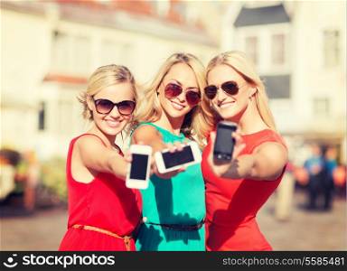 holidays and tourism, modern technology concept - beautiful blonde girls with smartphones in the city
