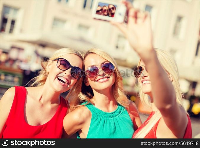 holidays and tourism, modern technology concept - beautiful girls taking picture with digital camera in the city