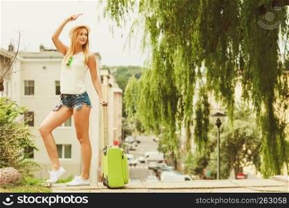 Holidays and vacation. Young smiling girl enjoy her freedom and summer time by travelling visiting other country city. Attractive woman with green suitcase.. Girl enjoy her free time holidays.