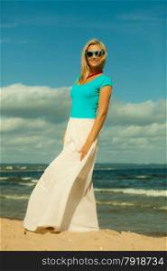 Holidays, beauty and summer fashion concept. Attractive blonde girl in full length walking on beach. Young woman relaxing on the sea shore.
