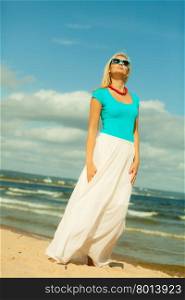 Holidays, beauty and summer fashion concept. Attractive blonde girl in full length walking on beach. Young woman relaxing on the sea shore.