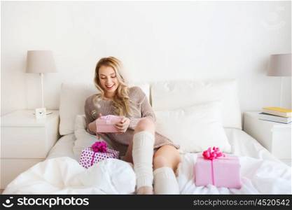 holidays, birthday, christmas morning and people concept - happy young woman gift boxes or presents in bed at home bedroom