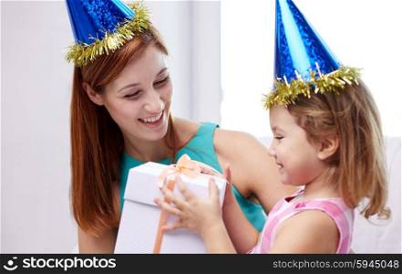 holidays, birthday family, childhood and people concept - happy mother and little girl in party caps with gift box at home