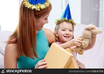 holidays, birthday, family, childhood and people concept - happy mother and little girl in party caps with gift box and toy at home