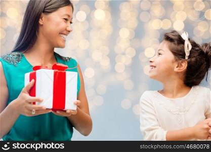 holidays, birthday family, childhood and people concept - happy mother giving present to her daughter rover holidays lights background