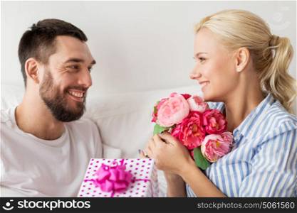 holidays, birthday, valentines day, romance and people concept - happy couple with gift box in bed at home. happy couple with gift box in bed at home