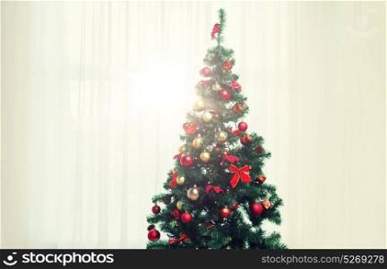 holidays, celebration and home concept - christmas tree in living room over window curtain. christmas tree in living room over window curtain