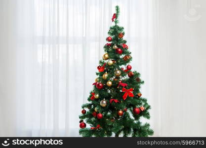 holidays, celebration and home concept - christmas tree in living room over window curtain