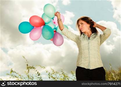 holidays, celebration and lifestyle concept - attractive woman female model holding bunch of colorful balloons outside cloudy sky background