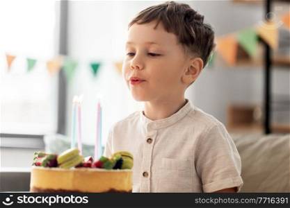 holidays, celebration and people concept - close up of happy little boy blowing candles on birthday cake at home party. happy little boy blowing candles on birthday cake