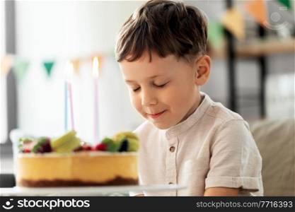 holidays, celebration and people concept - close up of happy little boy with birthday cake at home party making wish. happy little boy blowing candles on birthday cake