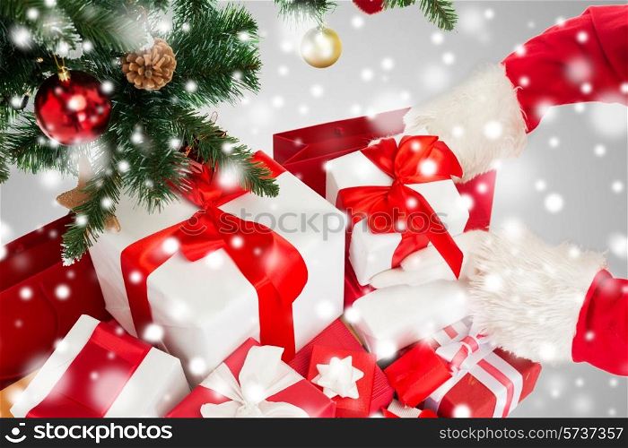 holidays, celebration and people concept - close up of santa claus putting present under christmas tree over gray background with snow