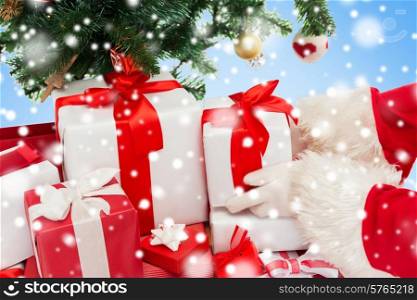 holidays, celebration and people concept - close up of santa claus putting present under christmas tree over blue background with snow