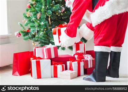 holidays, celebration and people concept - close up of santa claus putting present under christmas tree
