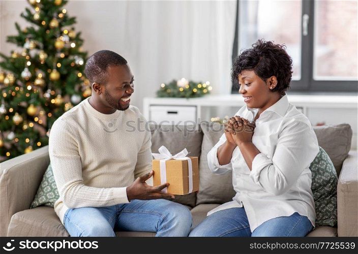 holidays, celebration and people concept - happy african american couple with christmas gift at home. happy african couple with christmas gift at home